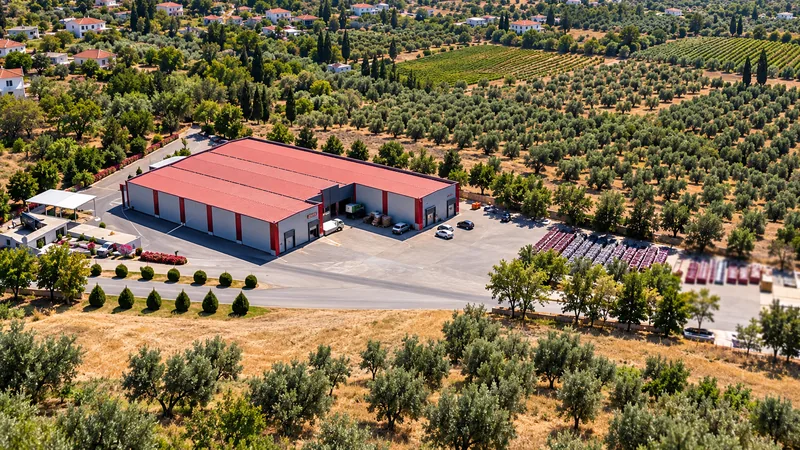 Aerial view of our production facility with a red roof, surrounded by olive groves and fields